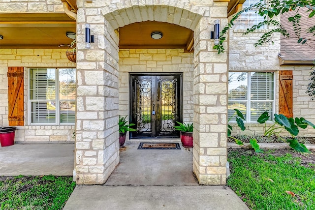 entrance to property featuring stone siding, french doors, and a shingled roof