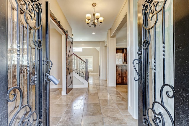 entrance foyer featuring a barn door, baseboards, an inviting chandelier, stairs, and stone tile flooring