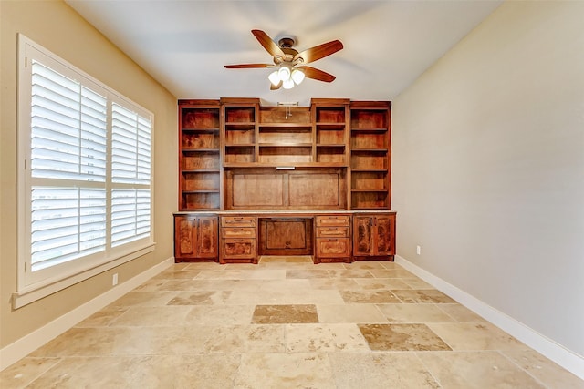 unfurnished office featuring stone finish flooring, ceiling fan, and baseboards