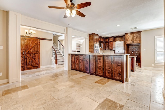 kitchen with visible vents, hanging light fixtures, a barn door, light stone countertops, and a peninsula