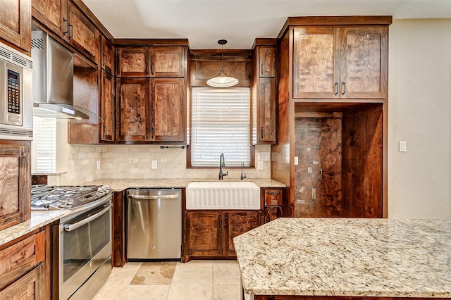 kitchen with wall chimney exhaust hood, light stone counters, decorative light fixtures, stainless steel appliances, and a sink