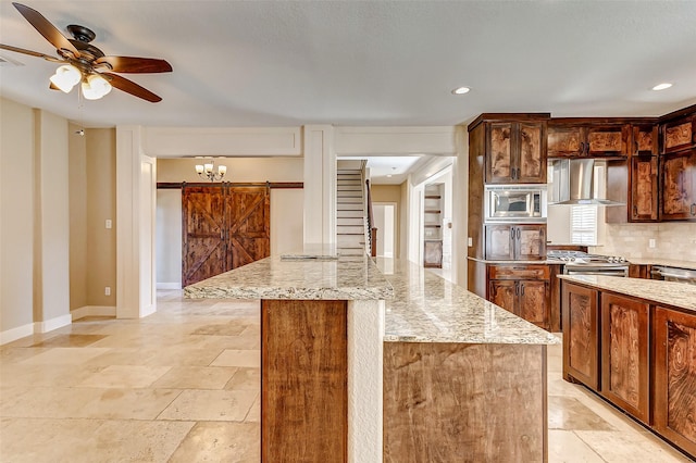 kitchen with a barn door, a kitchen island, baseboards, appliances with stainless steel finishes, and wall chimney exhaust hood