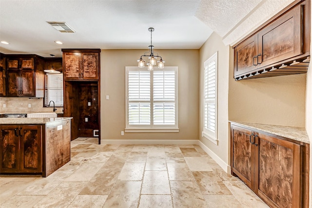 kitchen with visible vents, hanging light fixtures, backsplash, light stone countertops, and baseboards