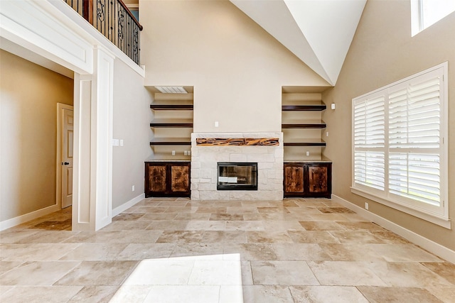 unfurnished living room featuring high vaulted ceiling, a glass covered fireplace, and baseboards