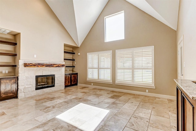 unfurnished living room featuring high vaulted ceiling, built in shelves, baseboards, and a stone fireplace