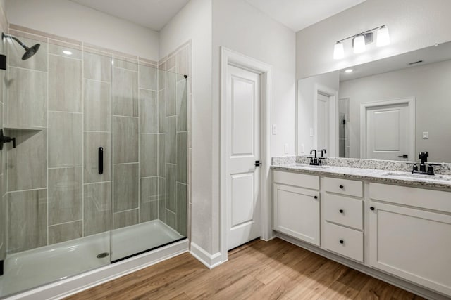 full bathroom featuring double vanity, a shower stall, a sink, and wood finished floors