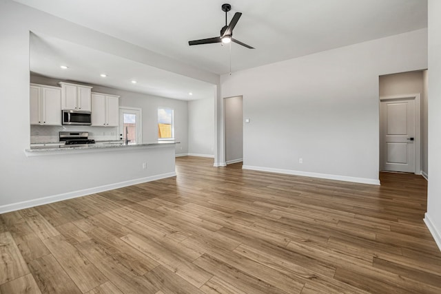 unfurnished living room featuring ceiling fan, recessed lighting, a sink, baseboards, and light wood-type flooring