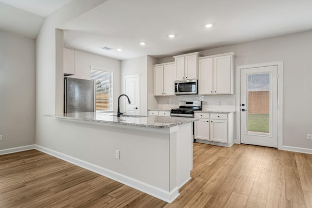 kitchen with light stone counters, light wood finished floors, appliances with stainless steel finishes, white cabinetry, and a sink