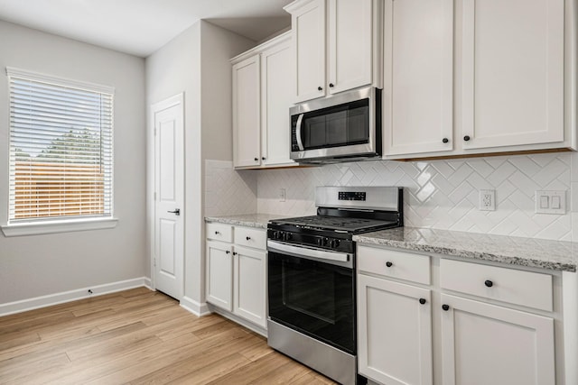 kitchen with light stone counters, stainless steel appliances, light wood-style floors, white cabinetry, and baseboards