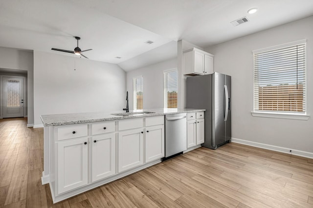 kitchen with light wood finished floors, stainless steel appliances, white cabinetry, a sink, and light stone countertops