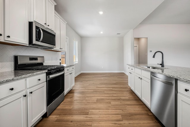 kitchen with a sink, white cabinets, appliances with stainless steel finishes, light wood-type flooring, and light stone countertops