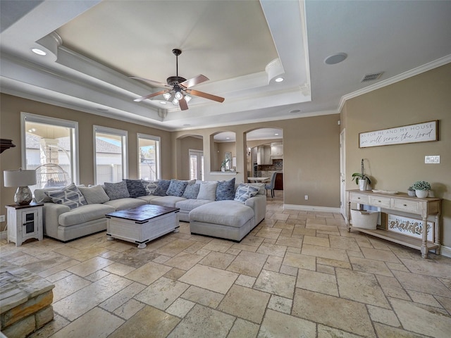 living room featuring visible vents, arched walkways, baseboards, a tray ceiling, and crown molding