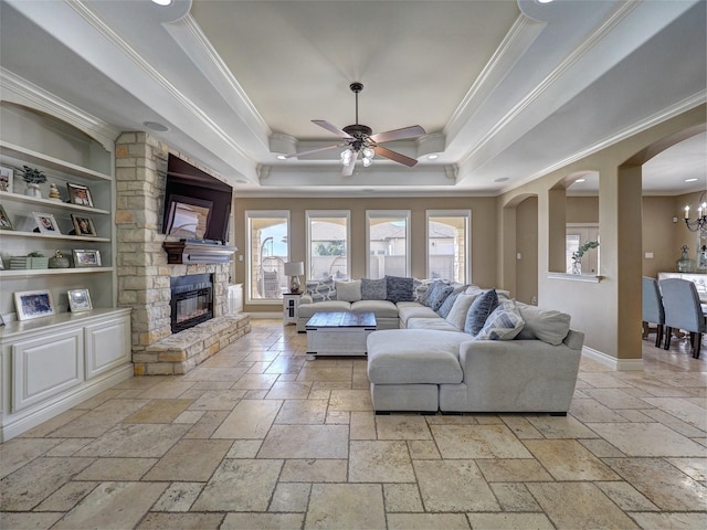 living area featuring ornamental molding, a tray ceiling, stone tile flooring, and a large fireplace