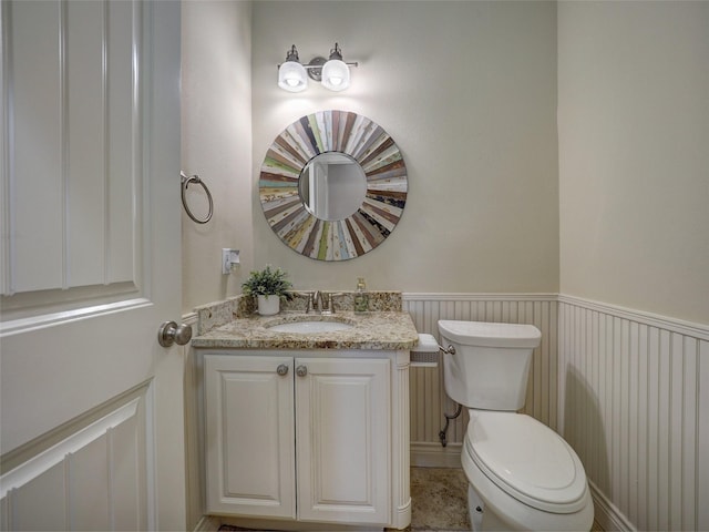 half bathroom with a wainscoted wall, vanity, and toilet