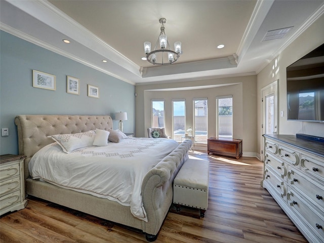 bedroom with a tray ceiling, crown molding, visible vents, an inviting chandelier, and wood finished floors