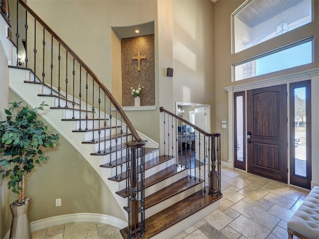 entryway featuring stone tile flooring, baseboards, and a high ceiling