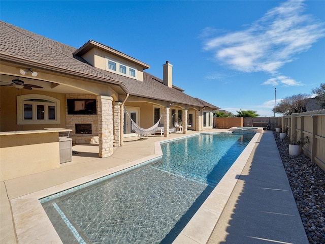 view of pool with a fenced backyard, ceiling fan, a patio area, a pool with connected hot tub, and an outdoor stone fireplace