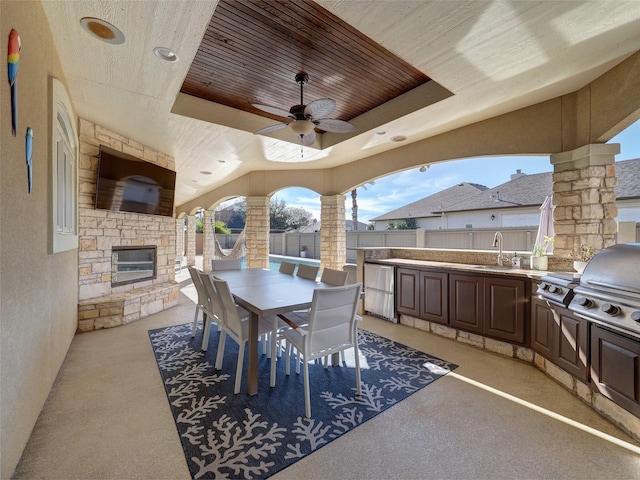 view of patio with outdoor dining area, a fenced backyard, an outdoor stone fireplace, a sink, and exterior kitchen