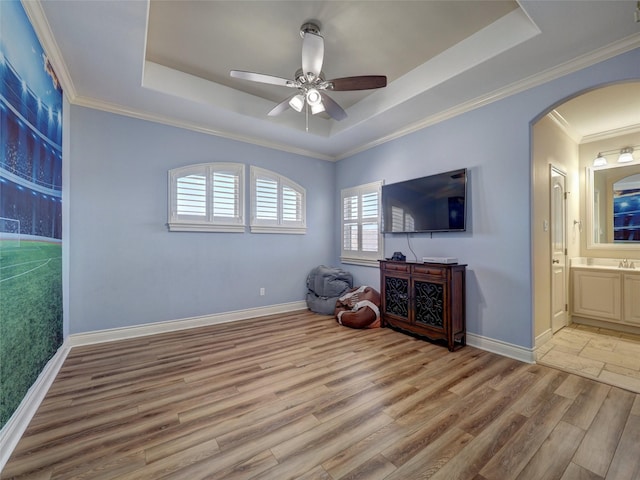 sitting room featuring light wood finished floors, baseboards, a tray ceiling, and arched walkways