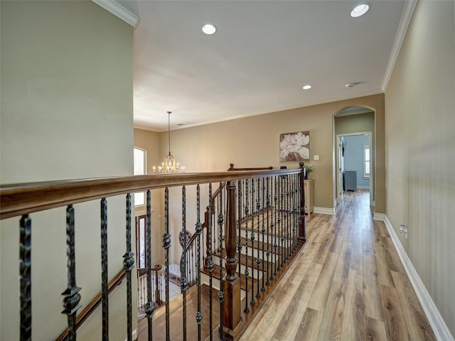 corridor featuring arched walkways, ornamental molding, light wood-style flooring, and baseboards