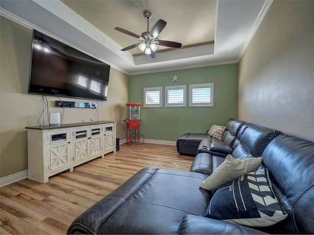 living area featuring baseboards, light wood-style flooring, ceiling fan, a tray ceiling, and crown molding