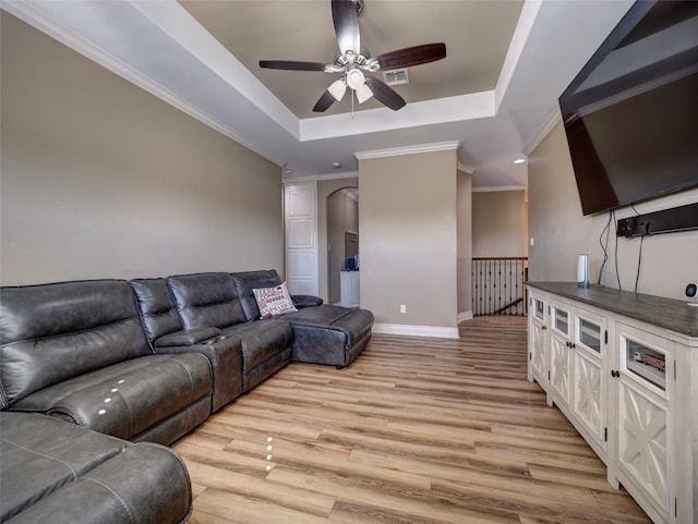 living room featuring arched walkways, visible vents, ornamental molding, a tray ceiling, and light wood finished floors