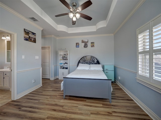 bedroom featuring light wood-style floors, crown molding, a raised ceiling, and a sink