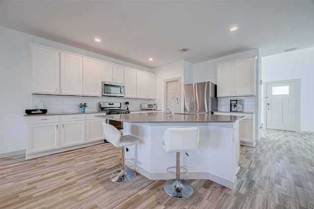 kitchen with white cabinets, a breakfast bar area, stainless steel appliances, and an island with sink