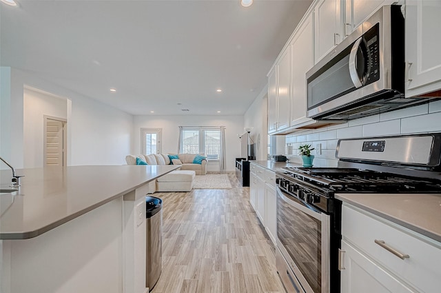 kitchen with light wood-style flooring, white cabinets, open floor plan, appliances with stainless steel finishes, and backsplash