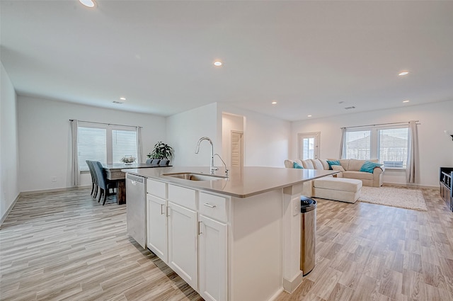 kitchen with light countertops, stainless steel dishwasher, open floor plan, a kitchen island with sink, and a sink