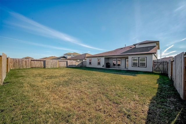 rear view of property featuring a yard and a fenced backyard