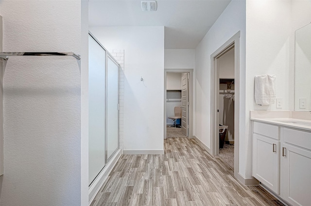 bathroom featuring a spacious closet, a stall shower, vanity, wood finished floors, and baseboards