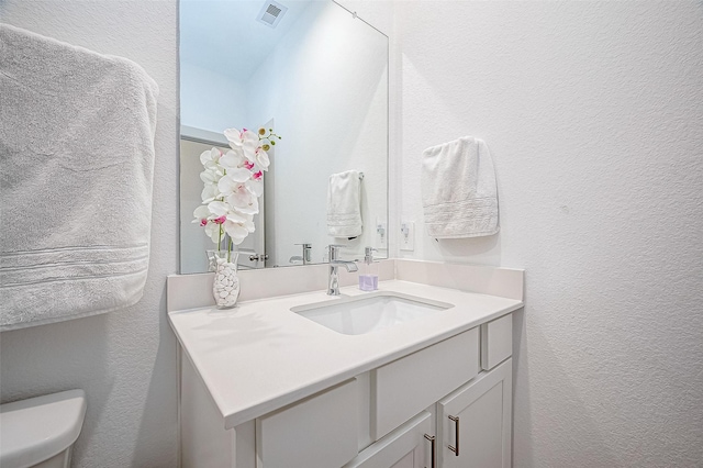 bathroom featuring toilet, a textured wall, vanity, and visible vents