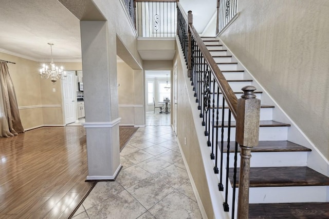 stairway with ornamental molding, wood finished floors, baseboards, and an inviting chandelier