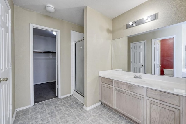 bathroom featuring toilet, vanity, baseboards, a spacious closet, and a shower stall