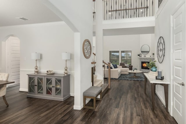 entryway featuring arched walkways, visible vents, a tiled fireplace, dark wood-type flooring, and crown molding