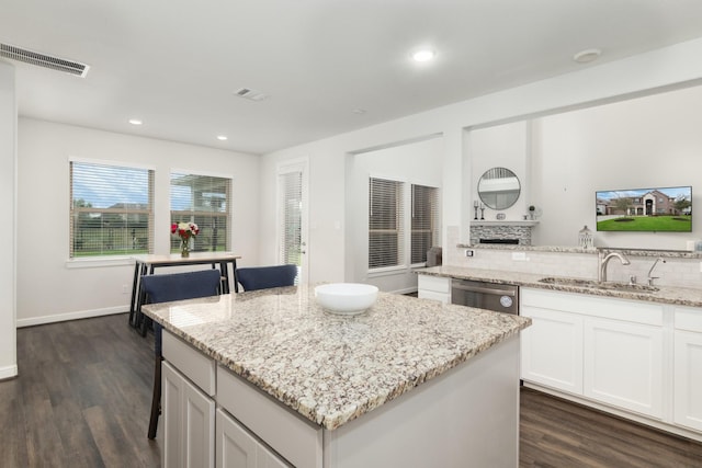 kitchen featuring a sink, visible vents, white cabinets, a kitchen breakfast bar, and a center island