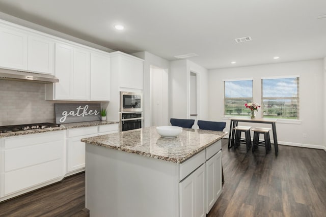 kitchen with light stone counters, visible vents, white cabinets, appliances with stainless steel finishes, and a center island