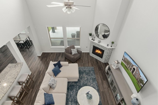 living room with a towering ceiling, baseboards, dark wood-type flooring, and a glass covered fireplace