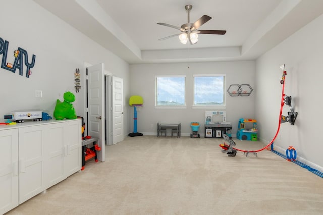 playroom with baseboards, ceiling fan, a tray ceiling, and light colored carpet