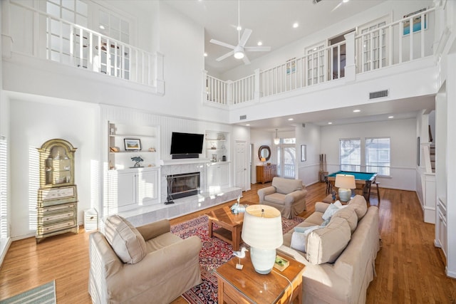 living room featuring a tiled fireplace, built in shelves, visible vents, and light wood finished floors