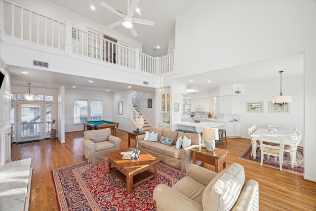 living room featuring visible vents, stairway, light wood-type flooring, ceiling fan with notable chandelier, and billiards