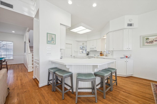 kitchen featuring white microwave, light countertops, white cabinets, a kitchen breakfast bar, and light wood-type flooring