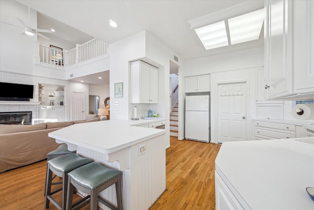 kitchen featuring white cabinetry, freestanding refrigerator, light wood-style floors, a peninsula, and a breakfast bar area