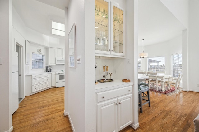 hall featuring baseboards, light wood-style floors, an inviting chandelier, and a skylight