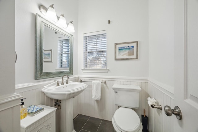 half bathroom with a sink, toilet, wainscoting, and tile patterned flooring