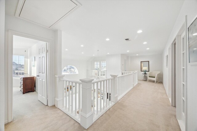 hallway featuring an upstairs landing, visible vents, light colored carpet, and attic access