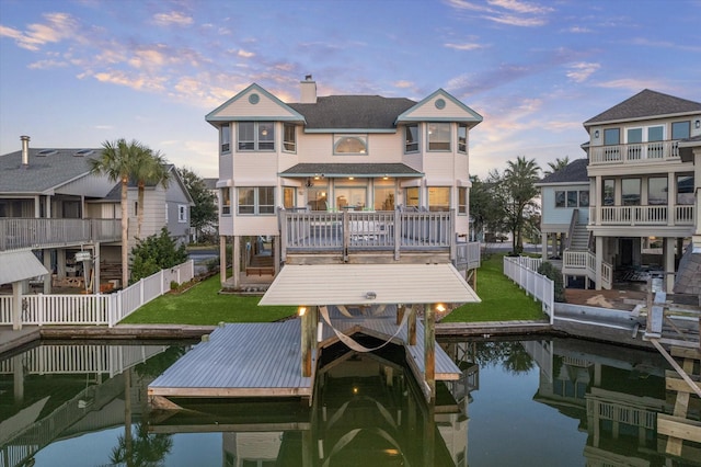 dock area with a deck with water view, a lawn, fence, and boat lift