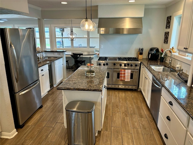 kitchen with a center island, stainless steel appliances, white cabinetry, a sink, and wall chimney exhaust hood