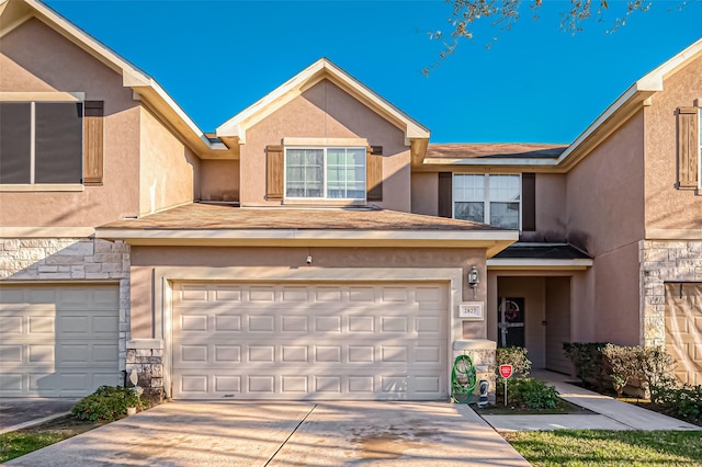 townhome / multi-family property with stone siding, driveway, an attached garage, and stucco siding